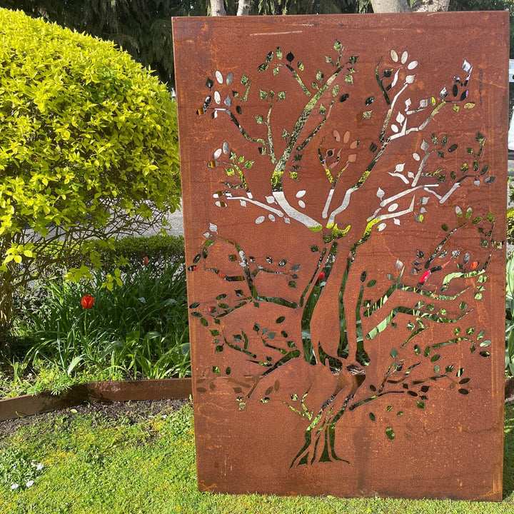 A brown metal decorative panel with a tree pattern, placed in a garden setting.
